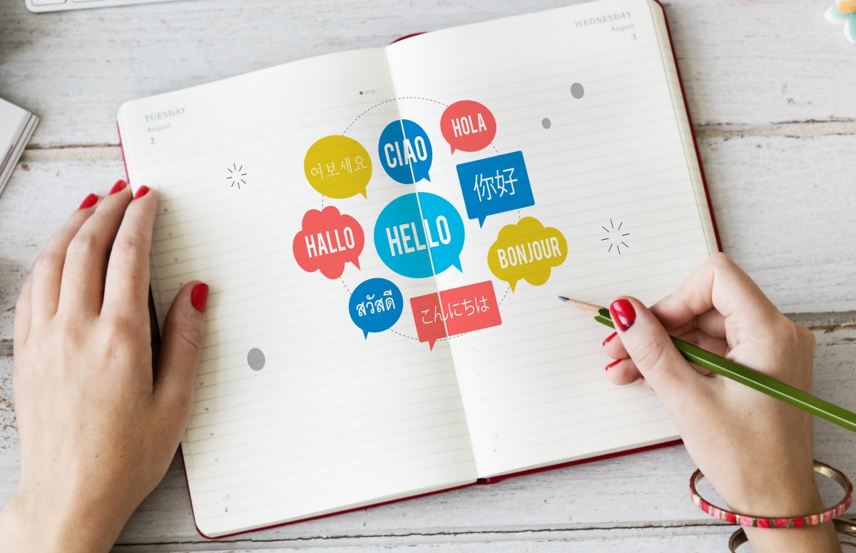 une jeune femme crayon à la main, note sur un cahier les expressions de differentes langues.