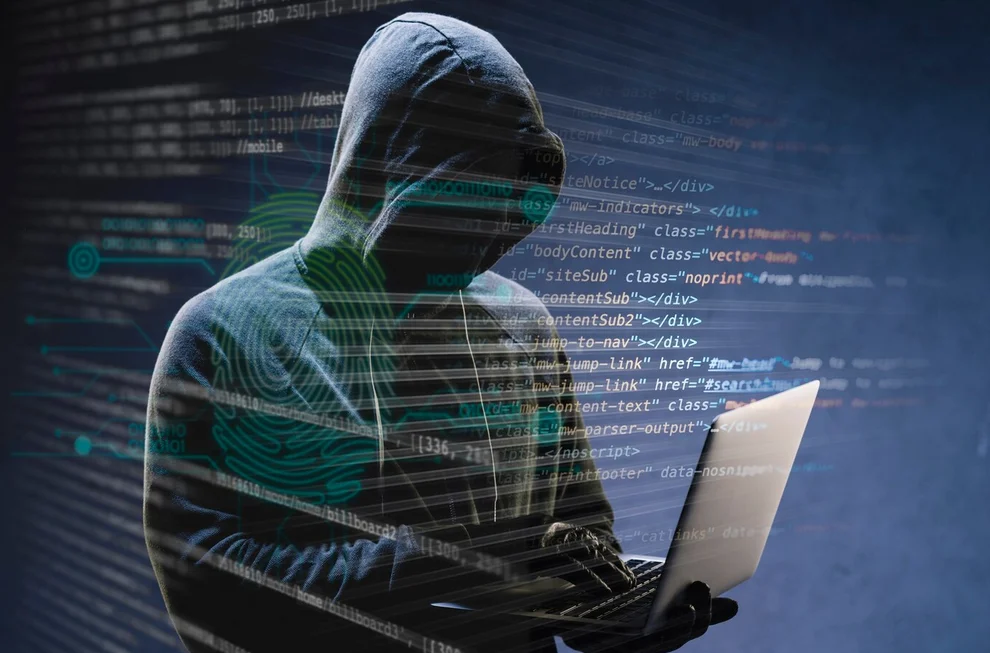 un cybercriminel cagoulé tente une intrusion un pc portable à la main.