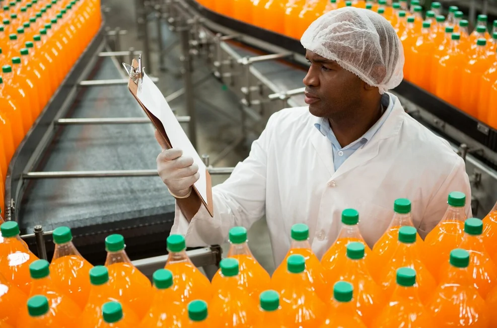Un technicien agroalimentaire contrôle la production de mise en bouteille d'une boisson orange defilant sur les rails.
