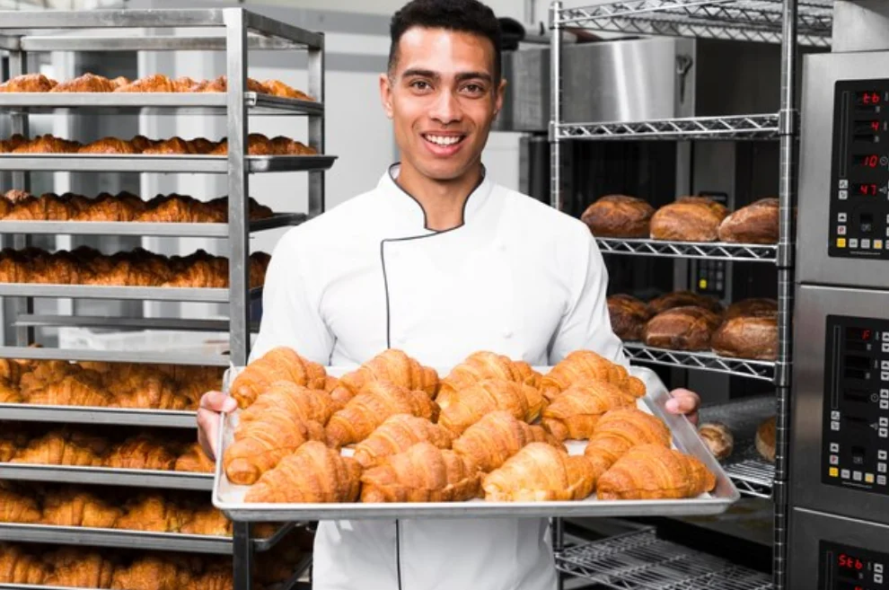 un boulanger-patissier présente un plateau de croissants sortis fraichement du four.